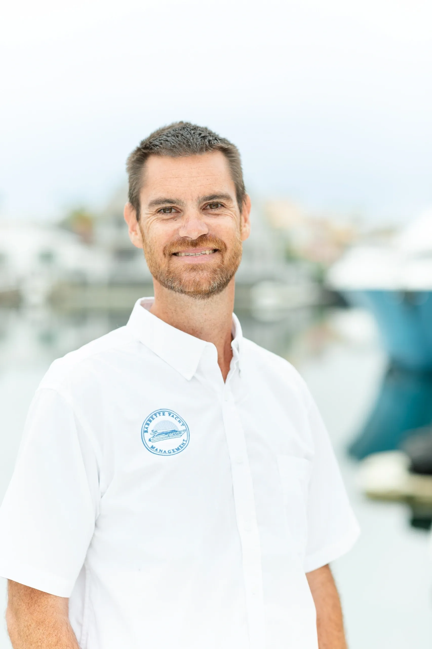 Man smiling near waterfront, wearing white shirt.