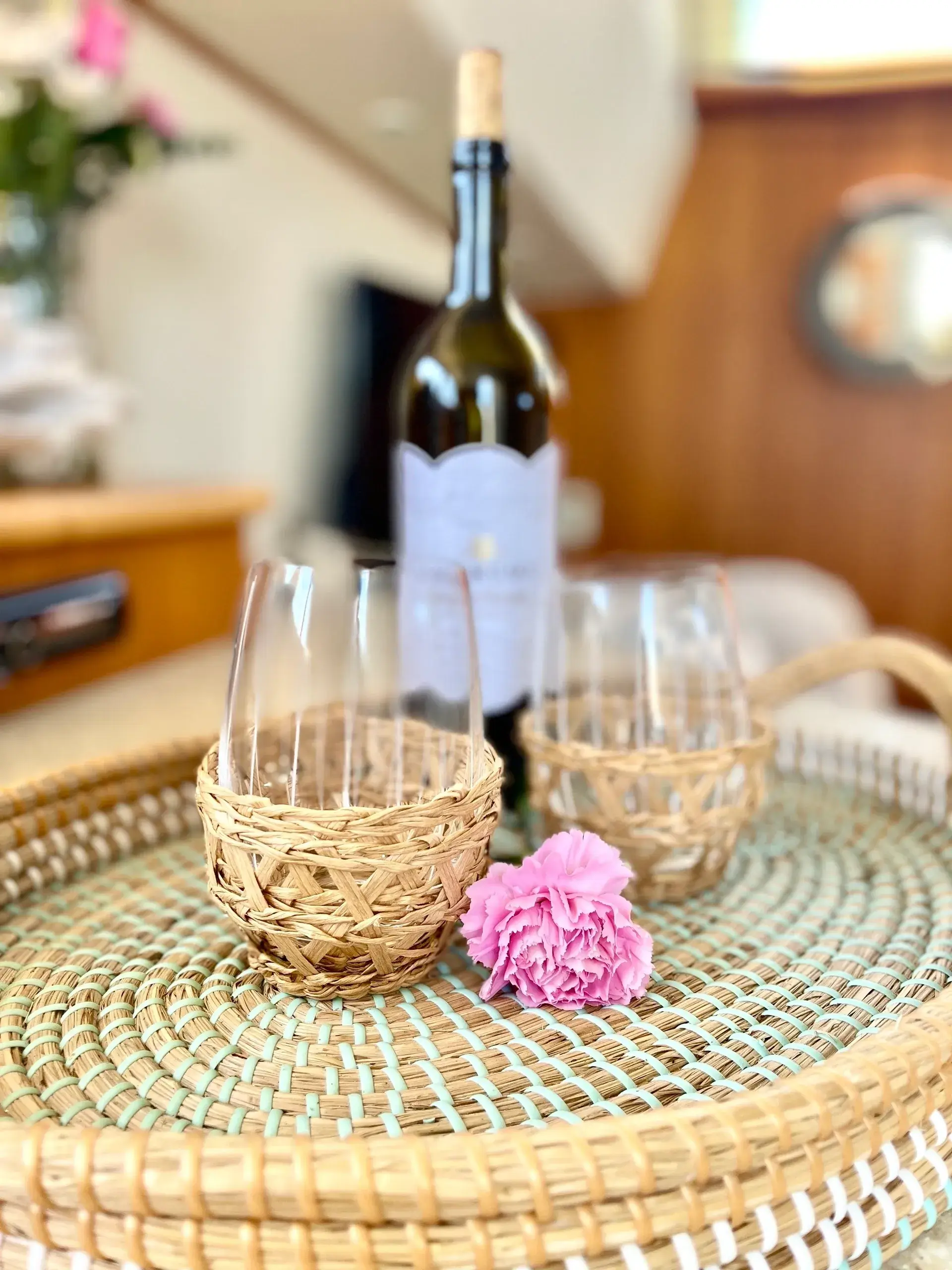 Wine bottle, glasses, and pink flower on tray.