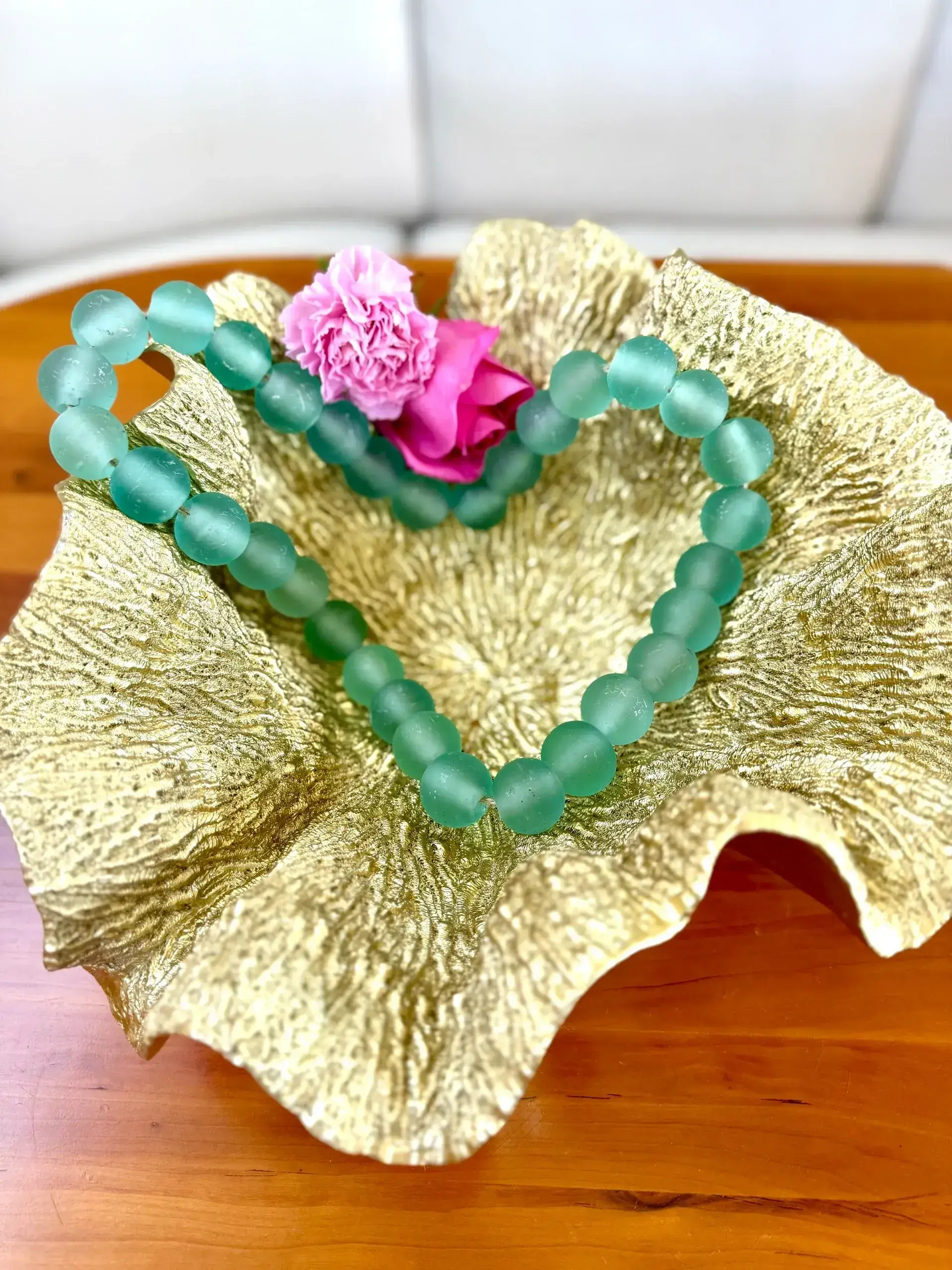 Green beads and flowers in gold dish.